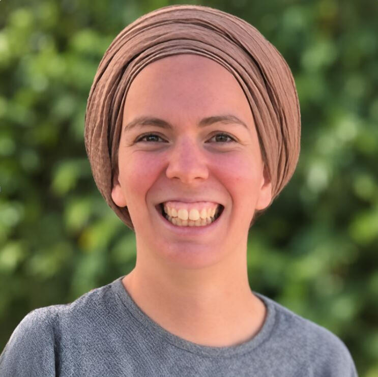 Portrait de Yemima, coach de vie, souriante et portant un turban beige sur fond de verdure.